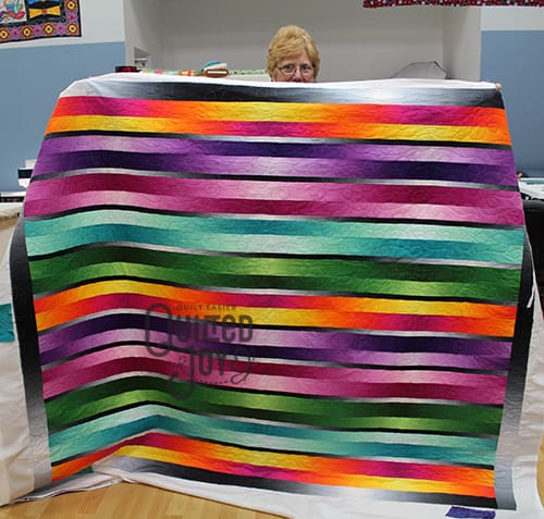 Carol shows off her ombre stripes quilt after renting a longarm machine at Quilted Joy